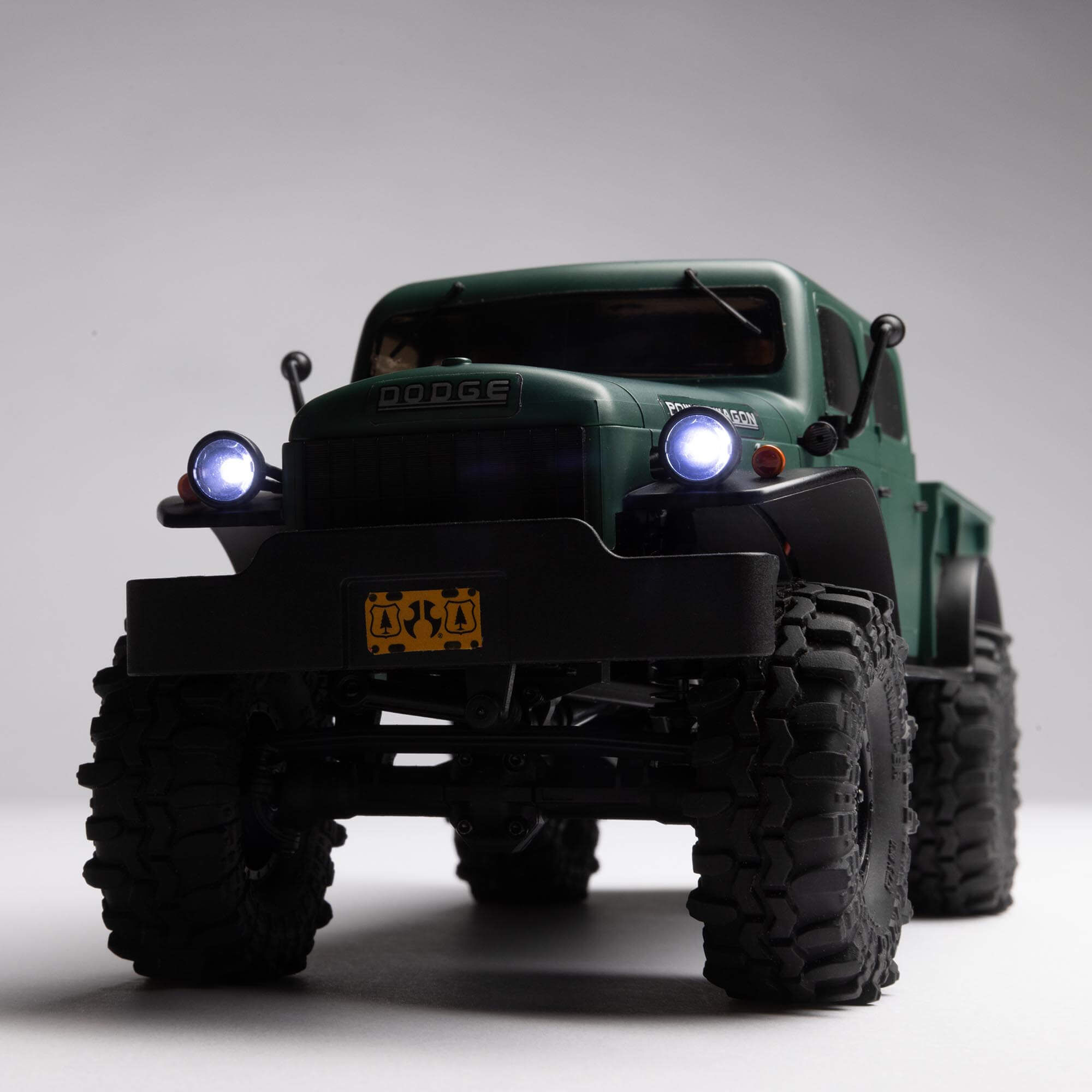 Official close front view of the green Axial SCX24 Power Wagon with its headlights illuminated
